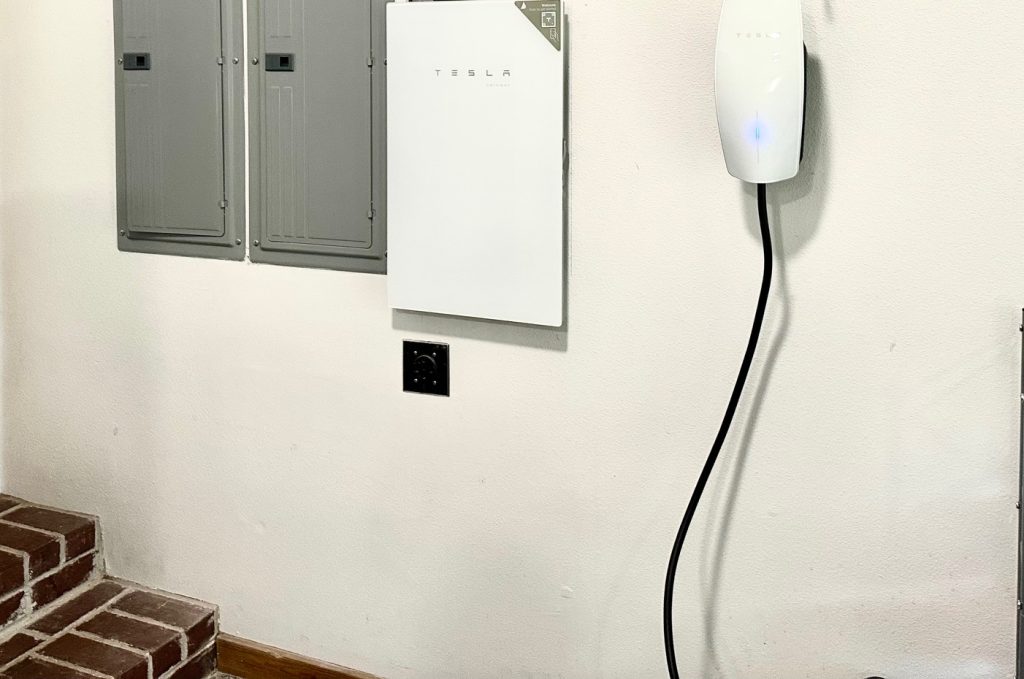 A Tesla wall charger installed near electrical panels in a home's garage.